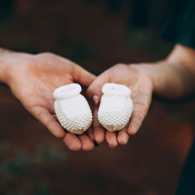 Two hands holding a pair of tiny white baby booties