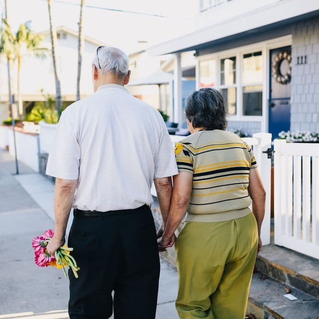 An older couple holding flowers behind their backs